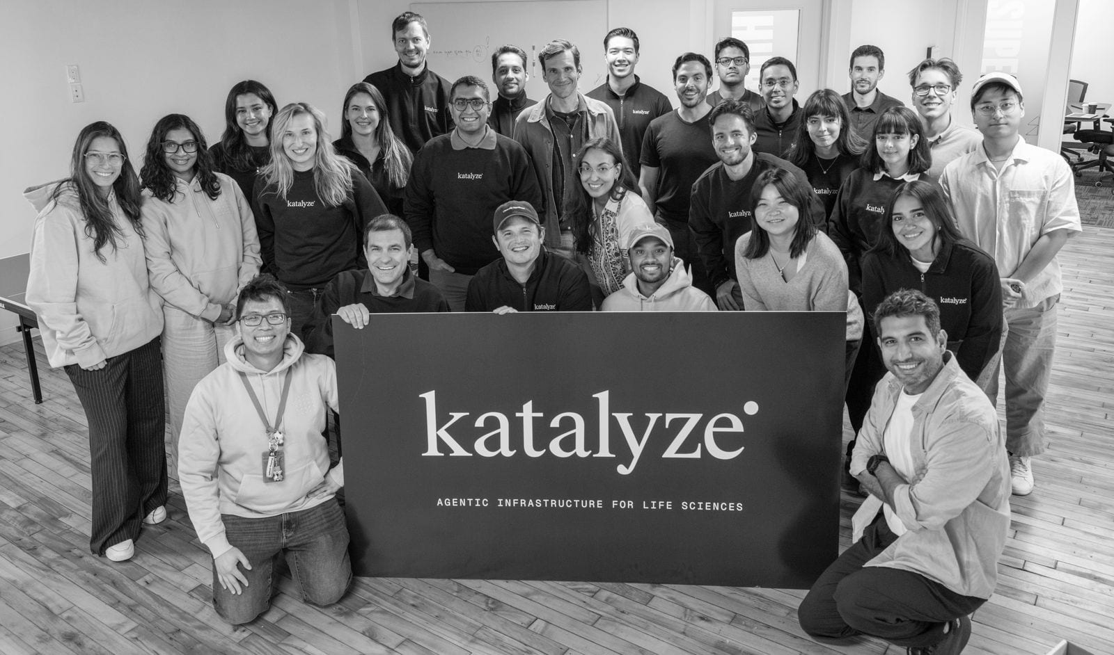 The Katalyze team in the office, around a sign that reads katalyze, agentic infrastructure for life sciences