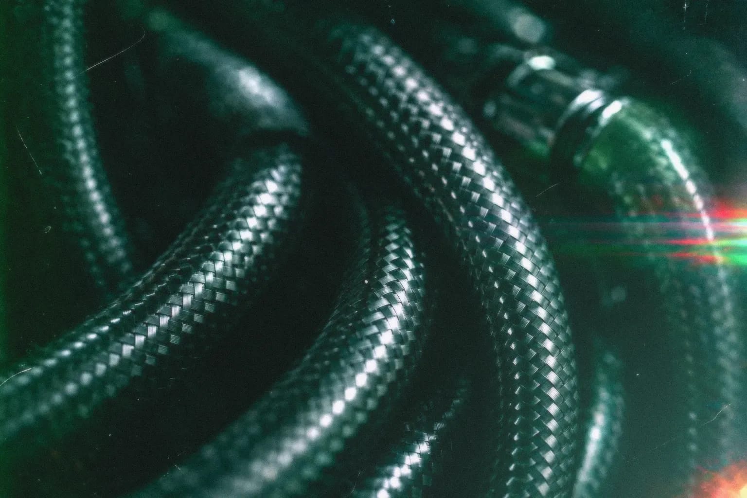 Coils of steel-braided hose glinting under dark green light